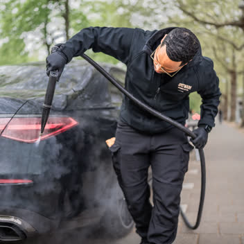 A detailer steam-cleaning the rear of a car on location.